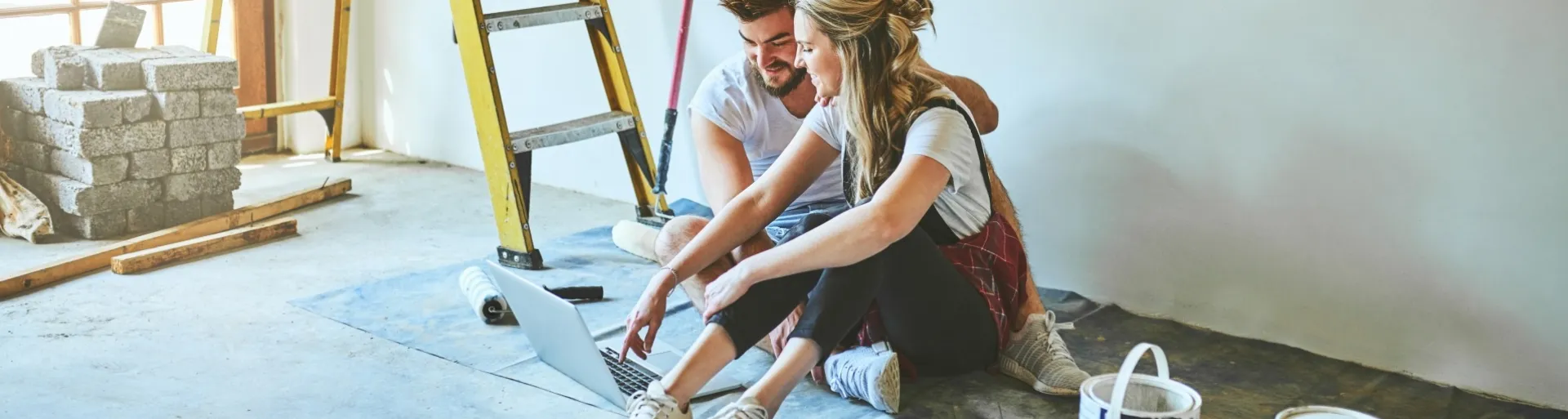 Jong stel zittend in nieuw huis met trap en verfpotten om zich heen